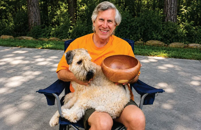 Russ sitting in a camp chair holding a mesquite bowl, with Baxter on his lap