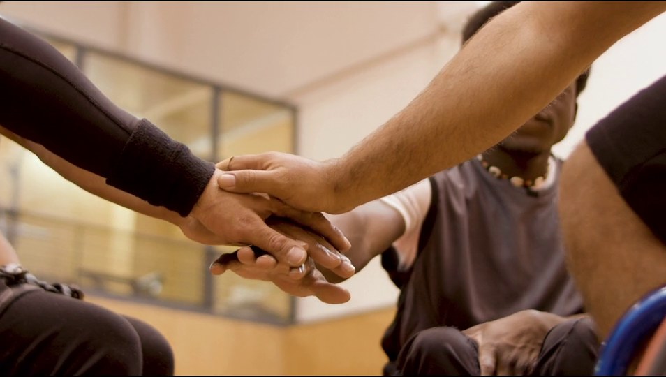 A wheelchair basketball team of players with different skin tones stacking their hands together before a game